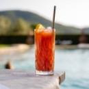 Cocktail rosso con ghiaccio e fetta di limone, accanto a una piscina.