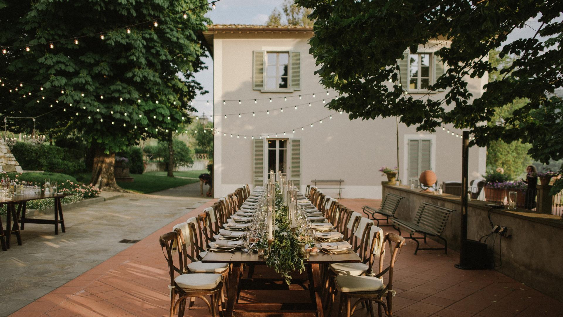 Tavolo elegante all'aperto, luci soffuse, atmosfera romantica e accogliente.