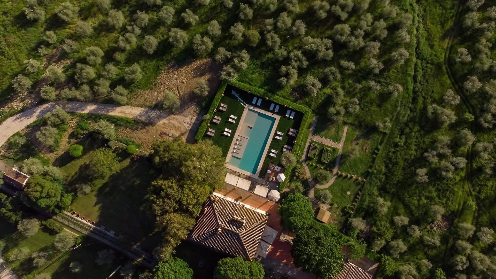 Vista aerea di una piscina rettangolare circondata da alberi e giardini verdi.