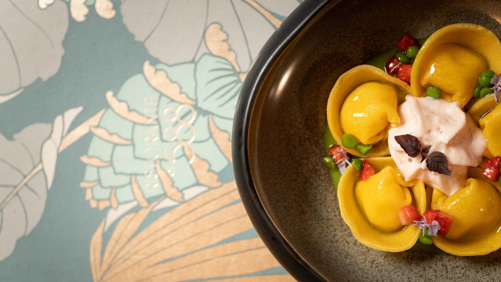Ravioli gourmet con crema e decorazioni floreali su piatto elegante.