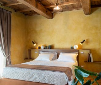 Camera da letto accogliente con pareti gialle, letto matrimoniale e travi in legno.