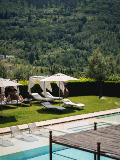 Piscina con lettini e ombrelloni, immersa nel verde delle colline circostanti.