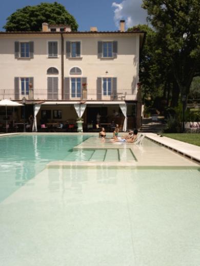 Villa storica con piscina, persone rilassate a bordo vasca in una giornata soleggiata.