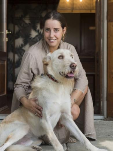 Donna sorridente accarezza un cane seduto davanti a una porta aperta.