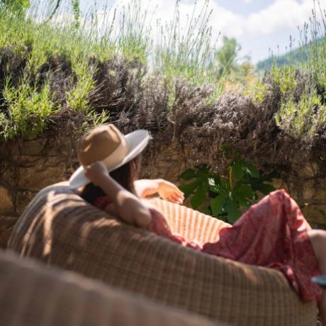 Persona rilassata su poltrona all'aperto, indossa cappello e abito rosso, natura circostante.