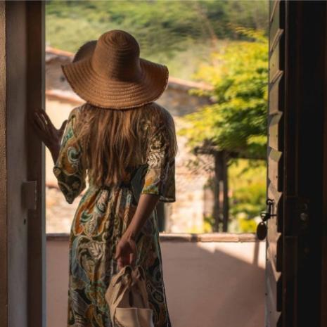 Donna con cappello di paglia guarda fuori da una porta verso un giardino soleggiato.