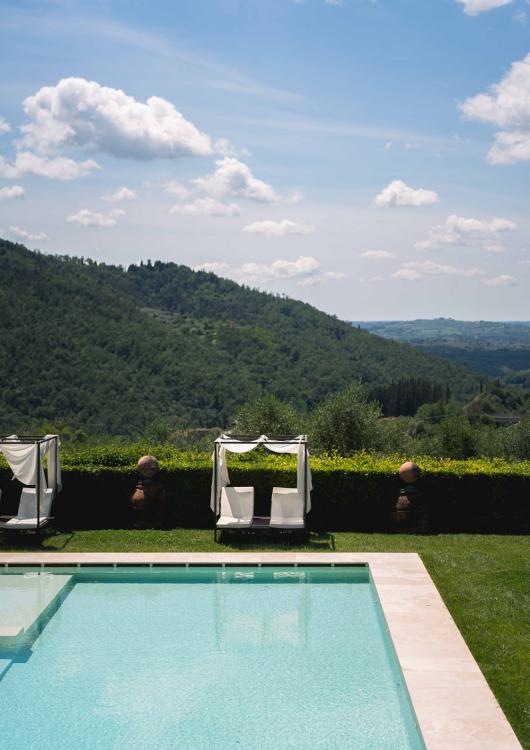 Piscina con vista su colline verdi e cielo azzurro con nuvole.