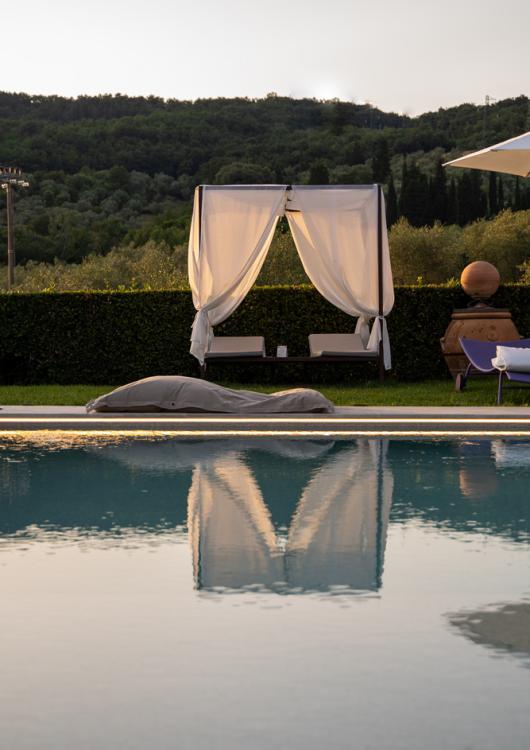 Piscina con baldacchino bianco e vista su colline verdi al tramonto.