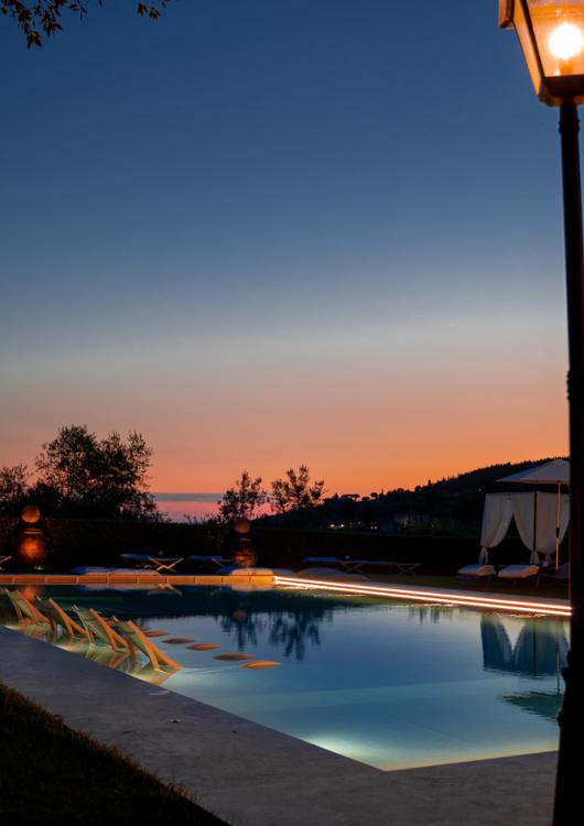 Piscina illuminata al tramonto con vista panoramica e arredi eleganti.