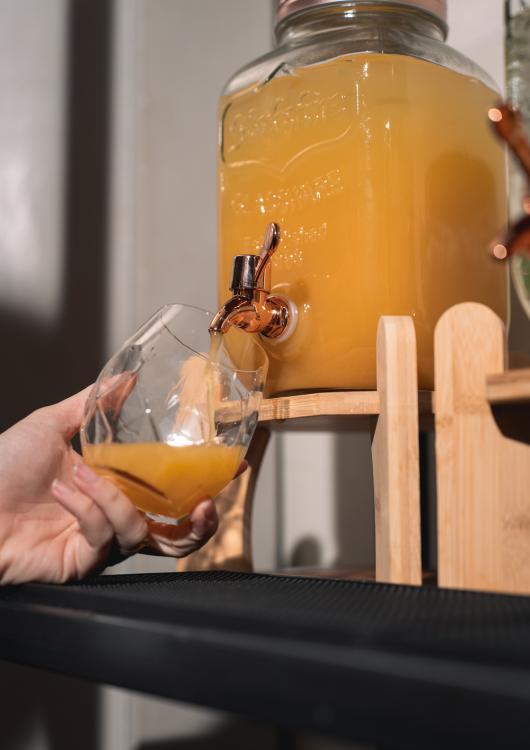 Dispenser di succo arancione con rubinetto, bicchiere in mano, versando la bevanda.