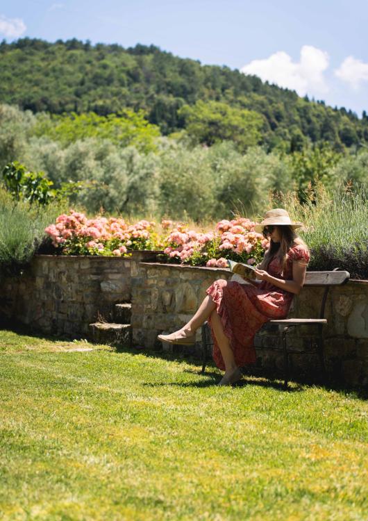 Donna legge su una panchina in giardino, circondata da fiori e natura.
