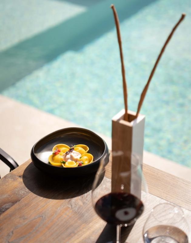 Piatto di pasta elegante con vino rosso, accanto a una piscina soleggiata.