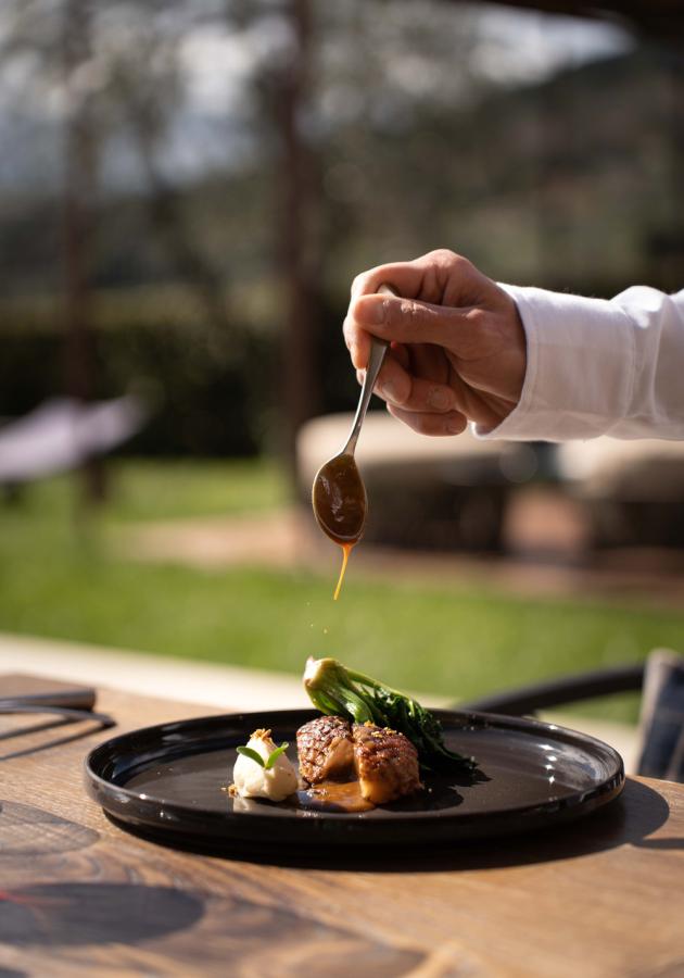 Chef versa salsa su piatto raffinato con carne e verdure al sole.