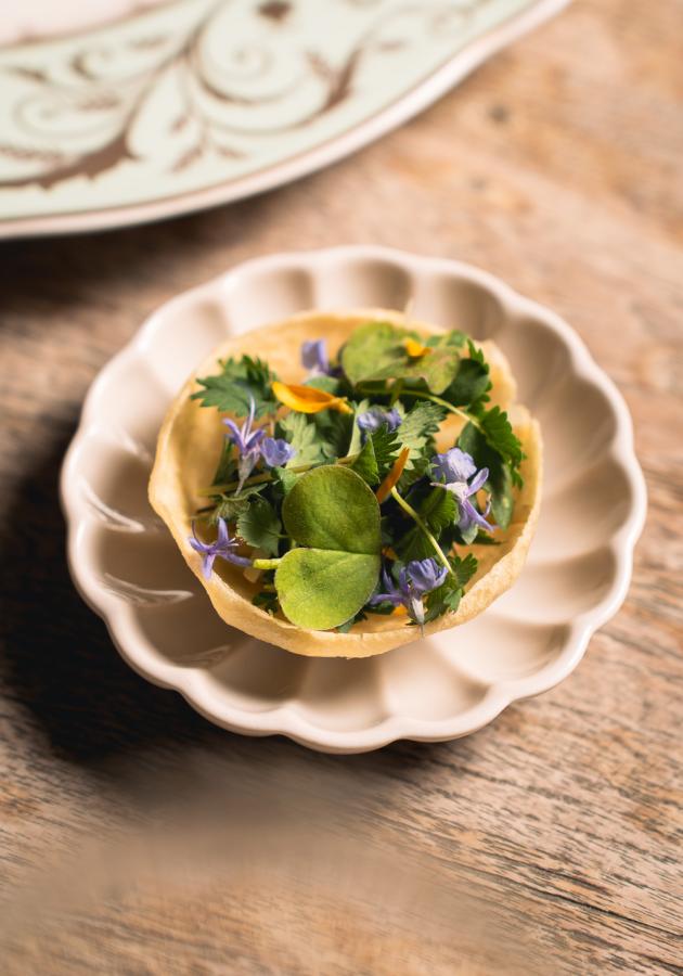 Tartina con erbe fresche e fiori, servita su piattino decorativo.