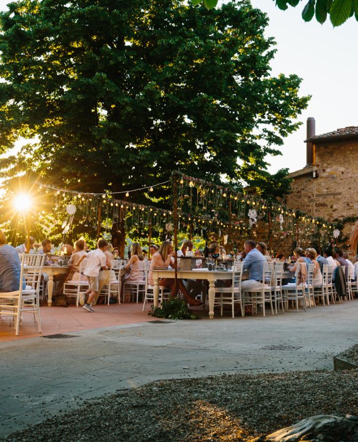 Cena all'aperto al tramonto, atmosfera festosa con luci e decorazioni.