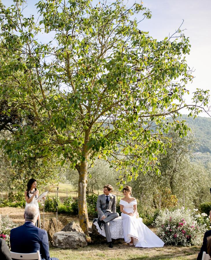 Cerimonia di matrimonio all'aperto con sposi seduti sotto un albero.